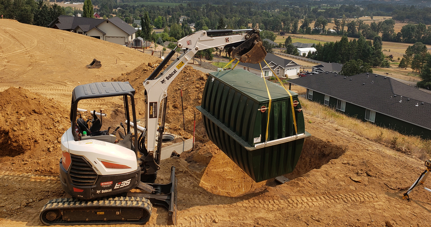Crane setting a concrete septic tank at a new home construction site