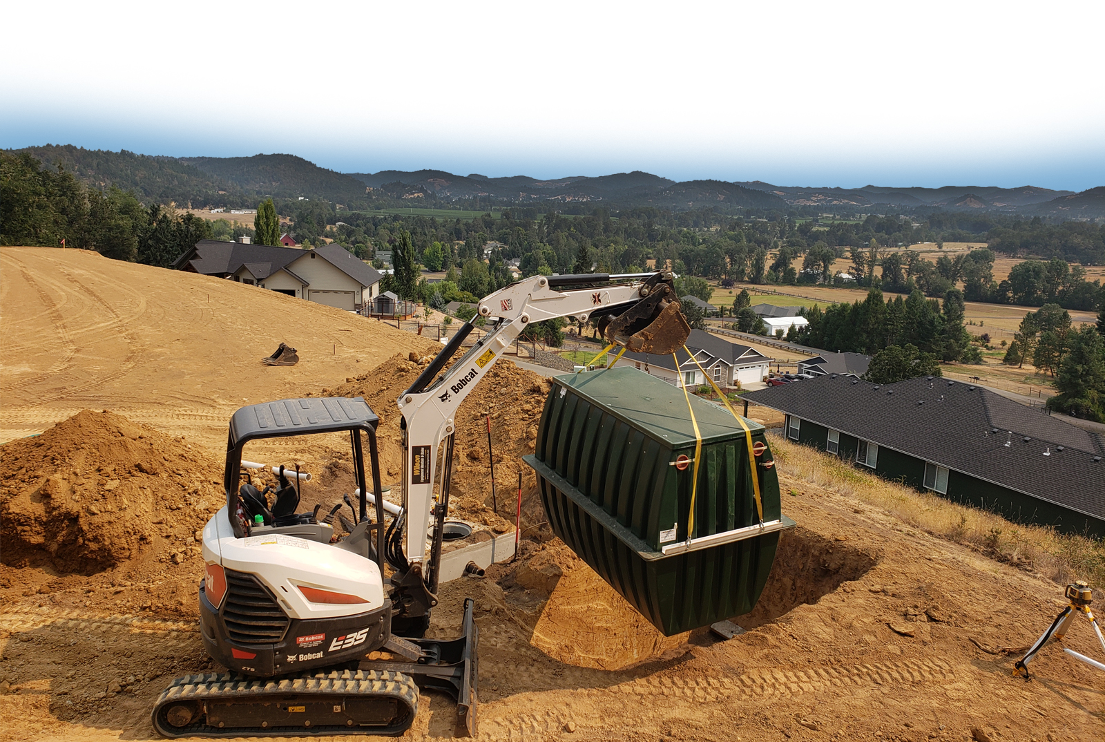 Excavator lowering a septic tank into the ground on a Douglas County hillside property
