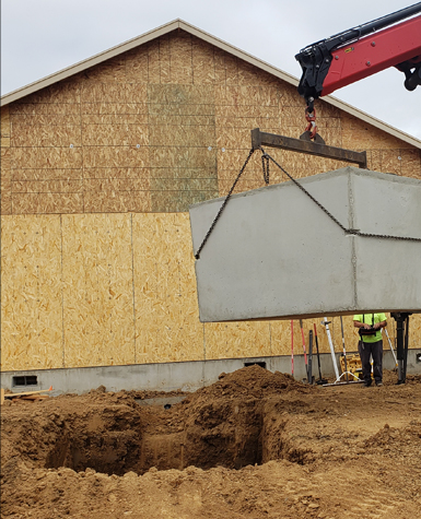 Crane setting a concrete septic tank at a new home construction site